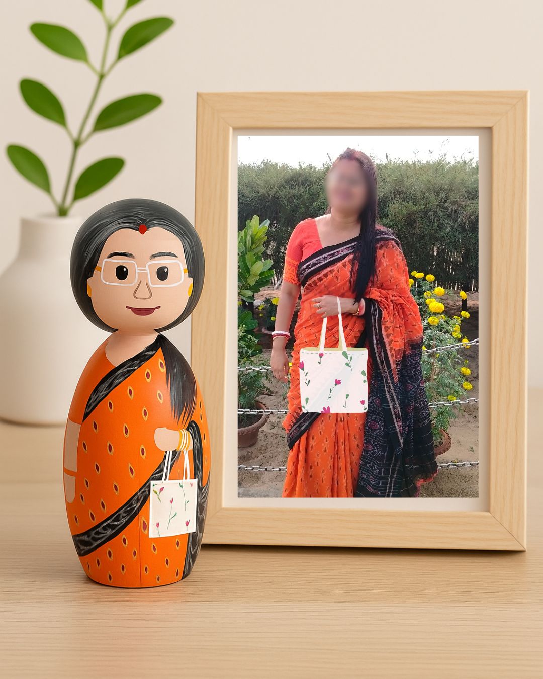 Decorative wooden peg doll of a woman in an orange saree next to a framed photo of a woman in a similar outfit outdoors.