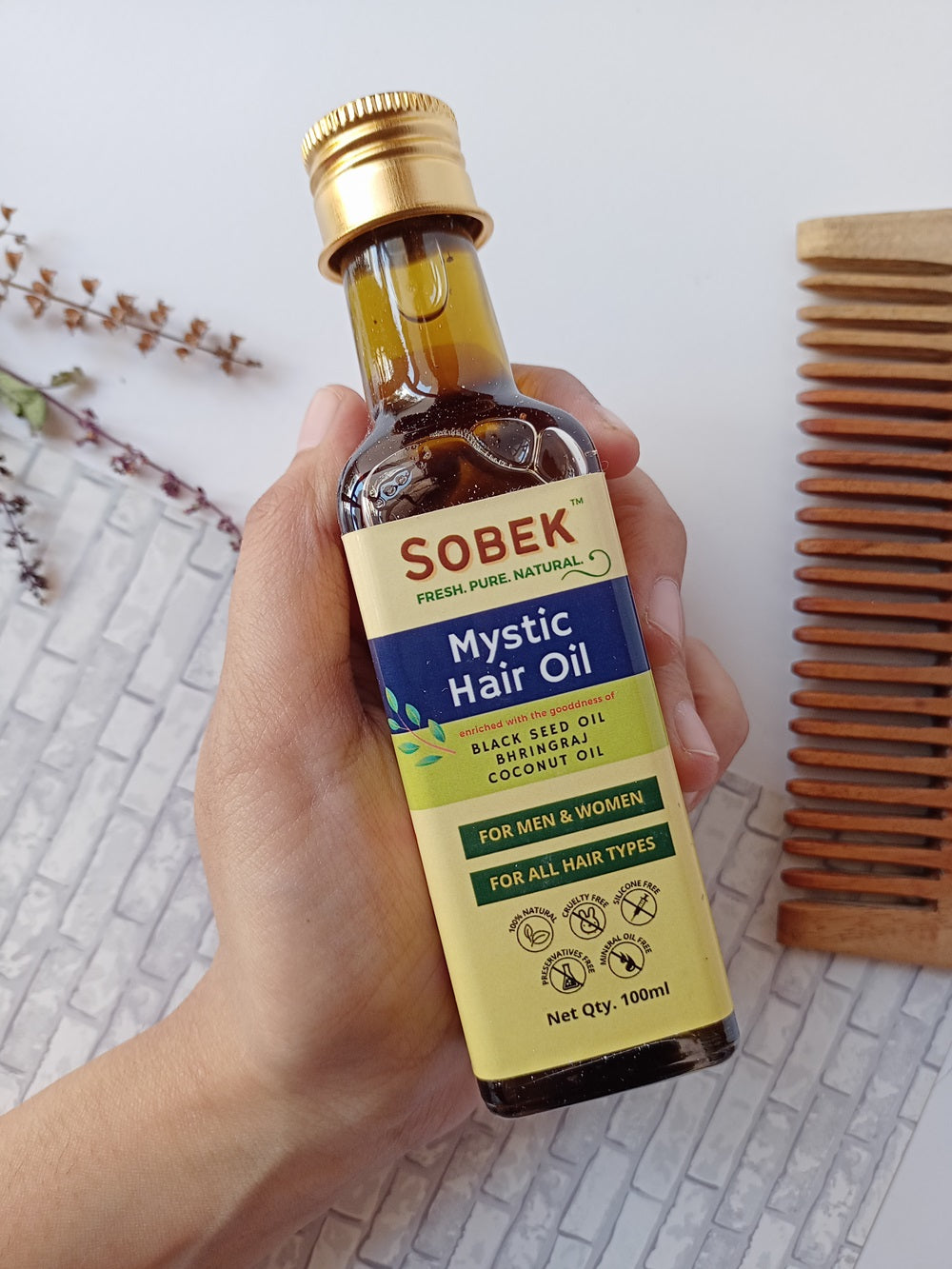 Hand holding sobek naturals mystic oil with brown box and leaves in the background