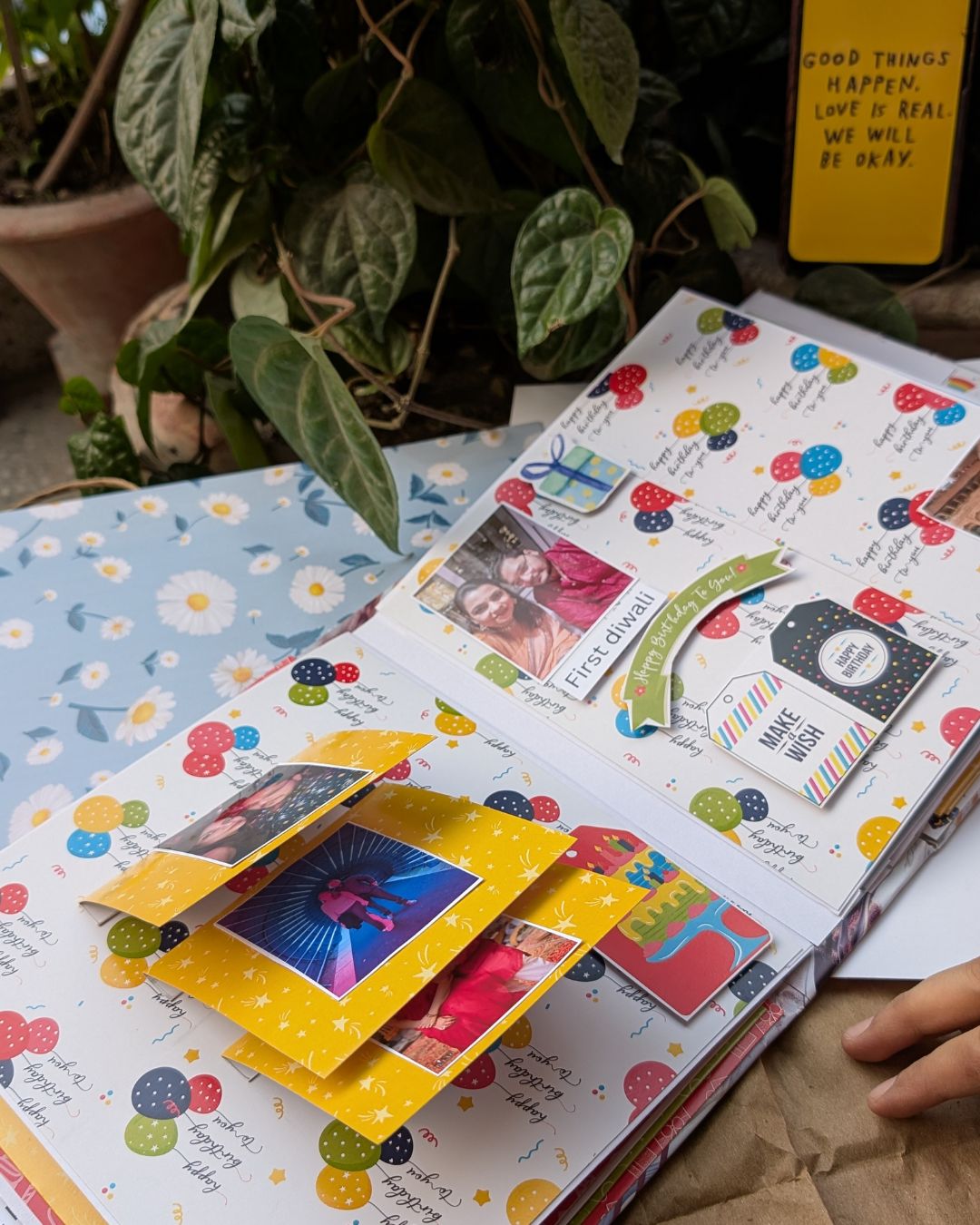 Open scrapbook with colorful pages and photos, surrounded by plants.