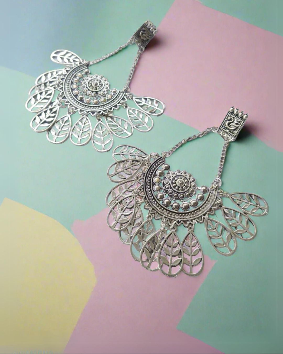 Silver jhumkas with leaf and swan pattern on a colorful backdrop