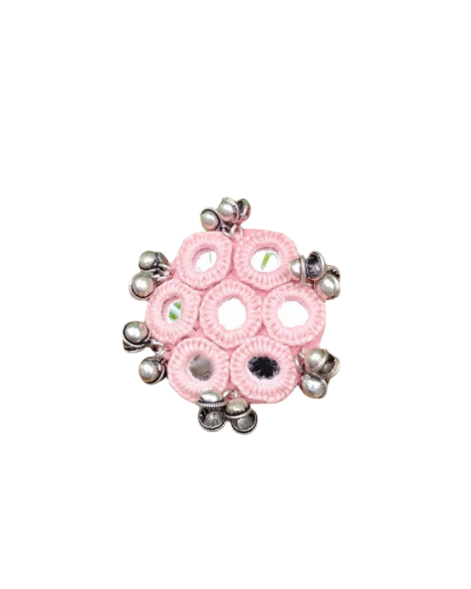 Pink crocheted ring with silver beads on a hand against a green leafy background