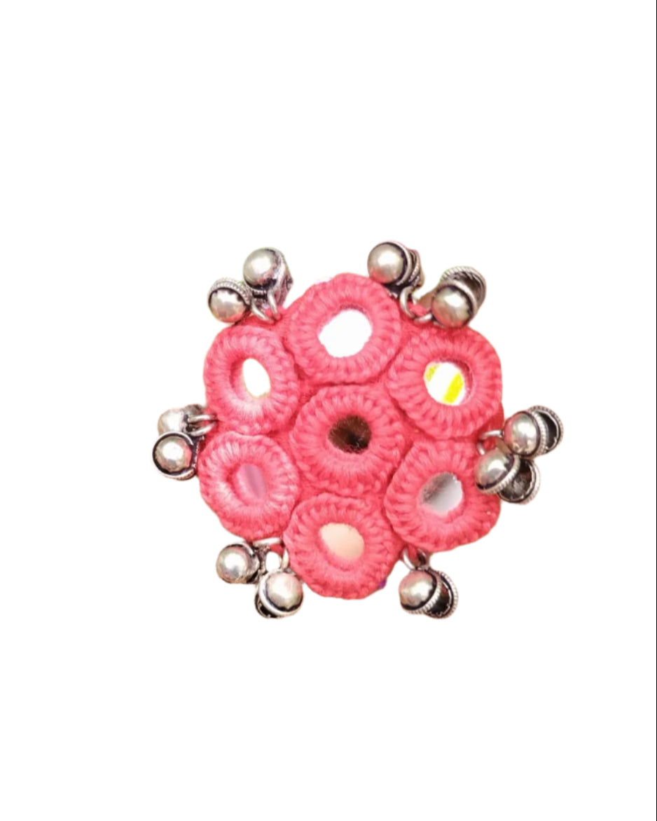 Hand wearing a pink beaded ring with green leaves in the background