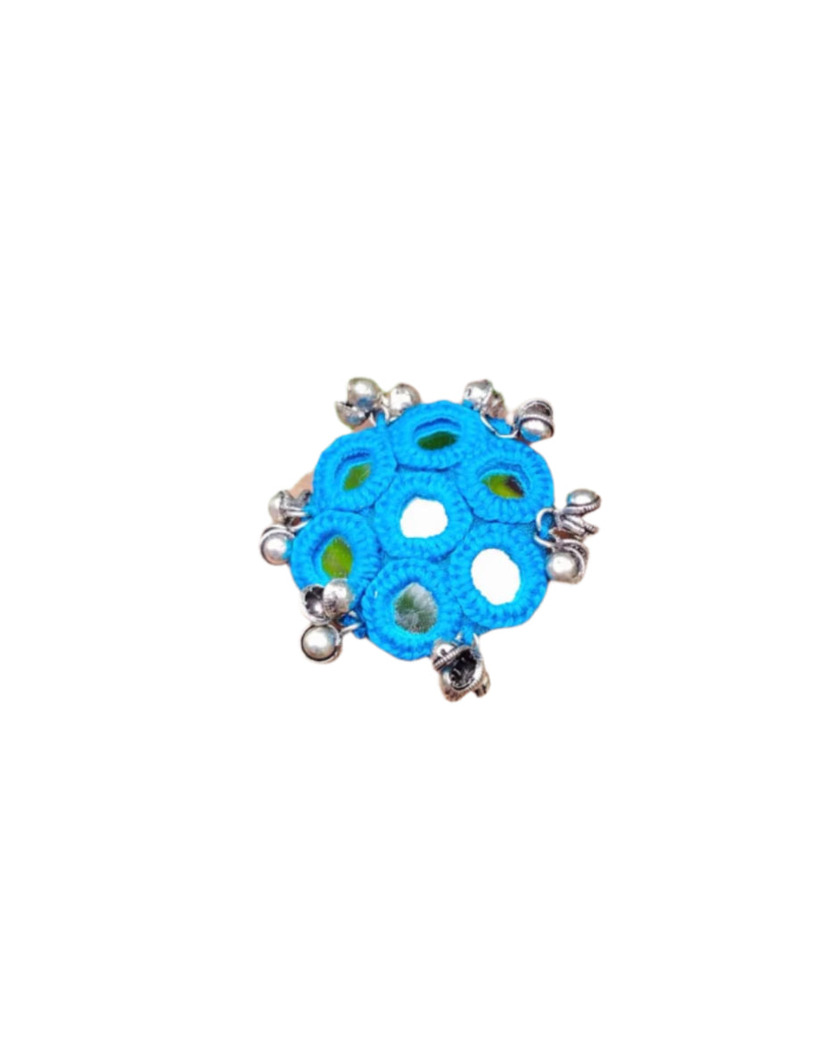 Hand wearing a blue ring with silver accents against a green leafy background