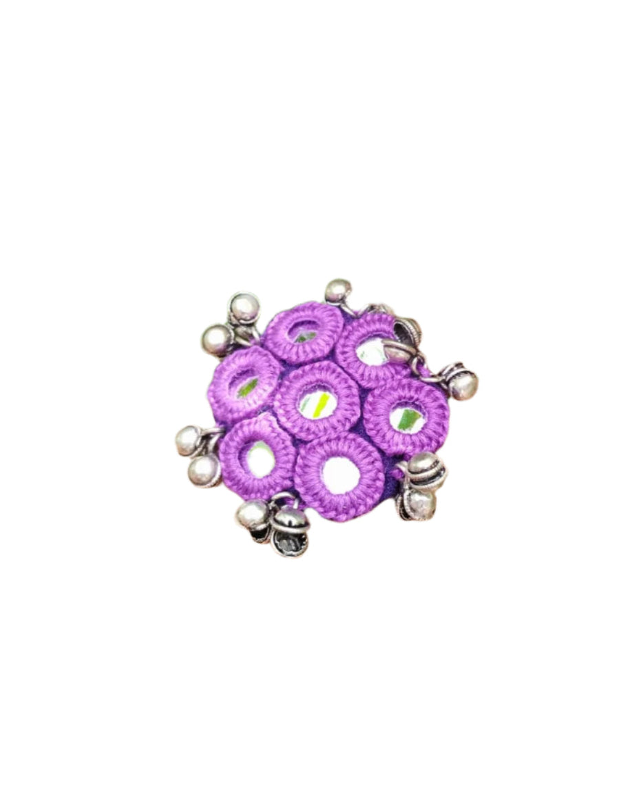 Hand wearing a purple beaded ring with green foliage in the background