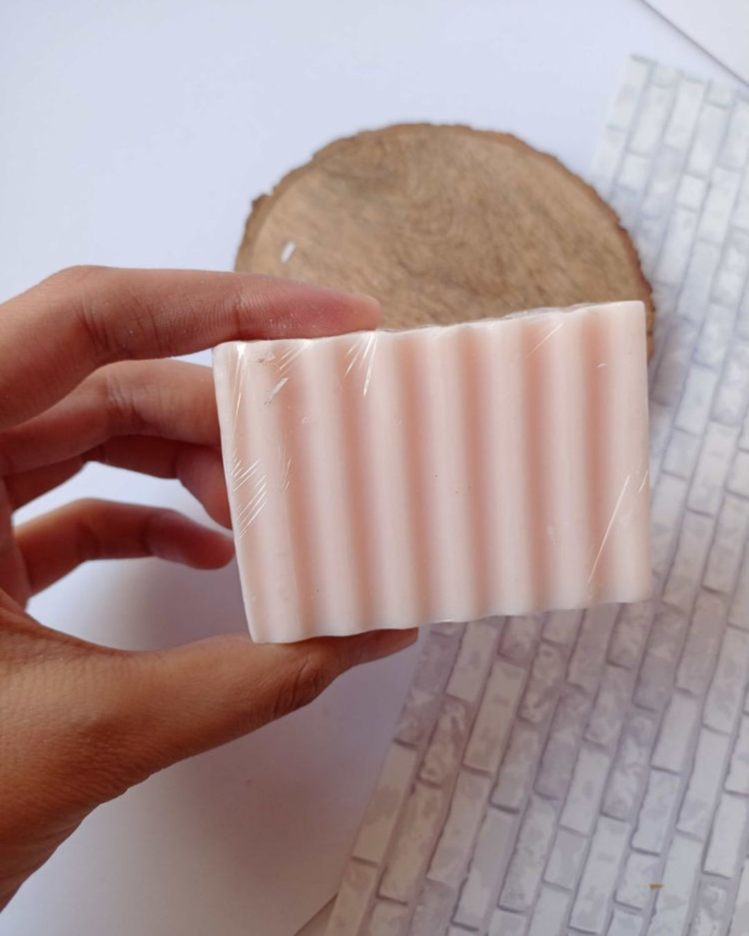 Hand holding pink rectangular soap bar on white grey backdrop