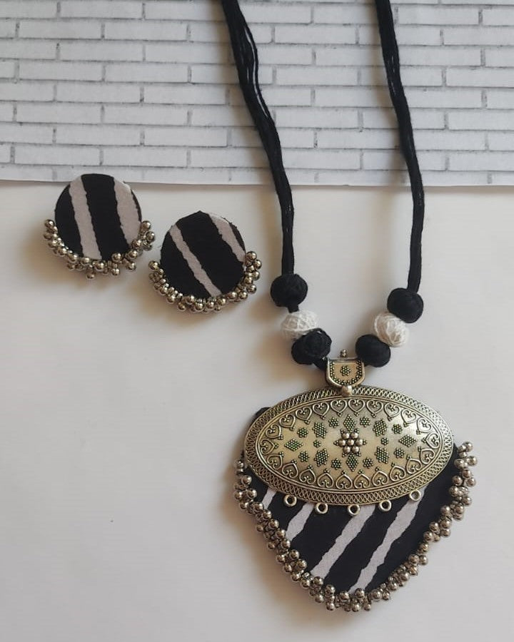 Black and white printed necklace and earrings set with silver locket on white backdrop