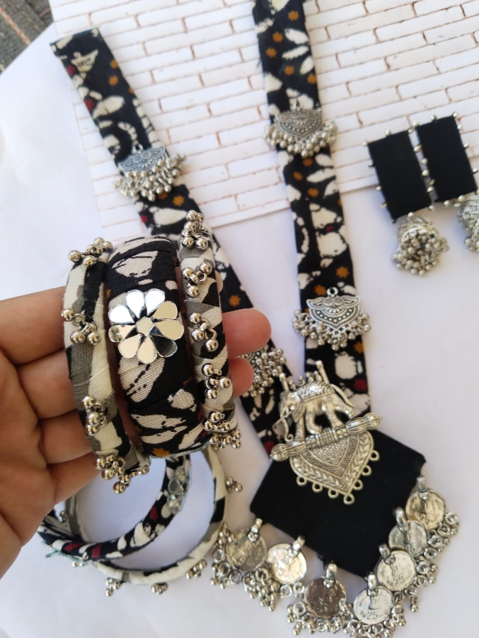 Hands with black fabric printed bangles, necklace and earrings set with silver details