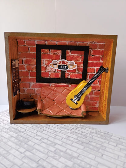 Wooden rectangular frame with miniature orange couch, guitar and friends theme background