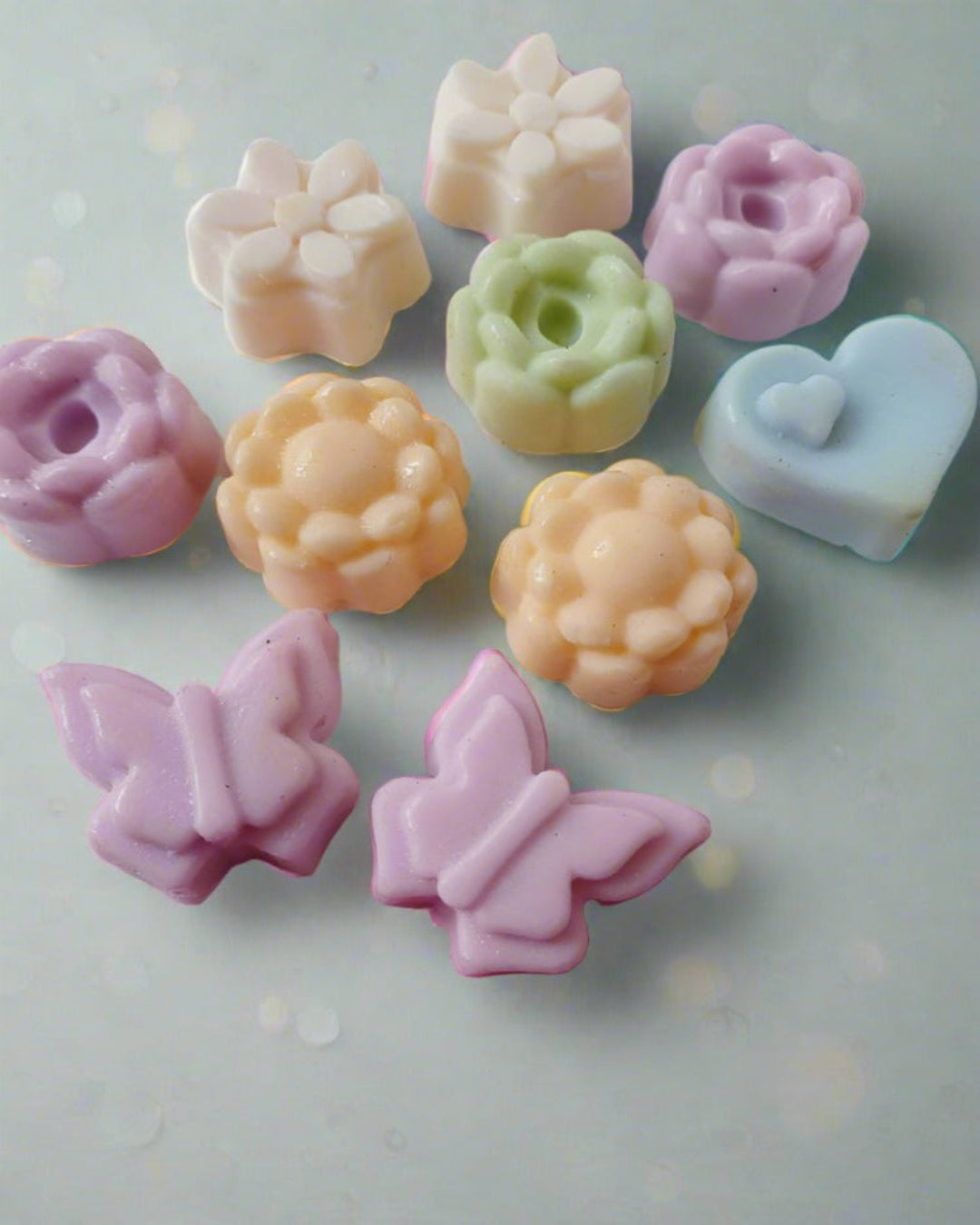 Mini flowers and butterfly shaped colorful soaps on white pink backdrop