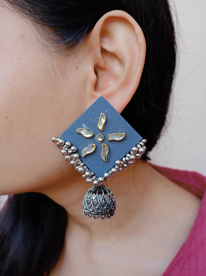 Close up of an ear of a girl wearing dusky blue kite shaped earrings with silver jhumki at bottom