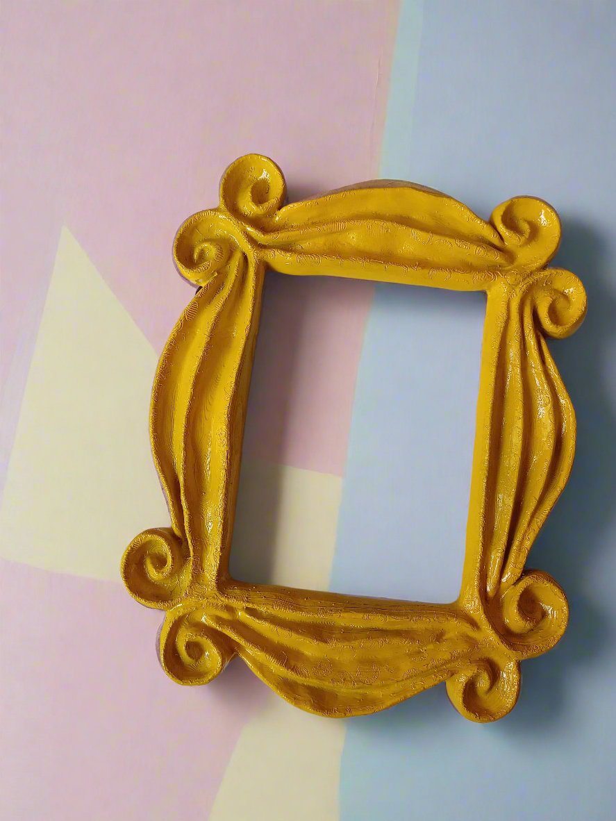A gold-colored wooden peephole frame with decorative details, placed against a background with geometric shapes in pink and blue.