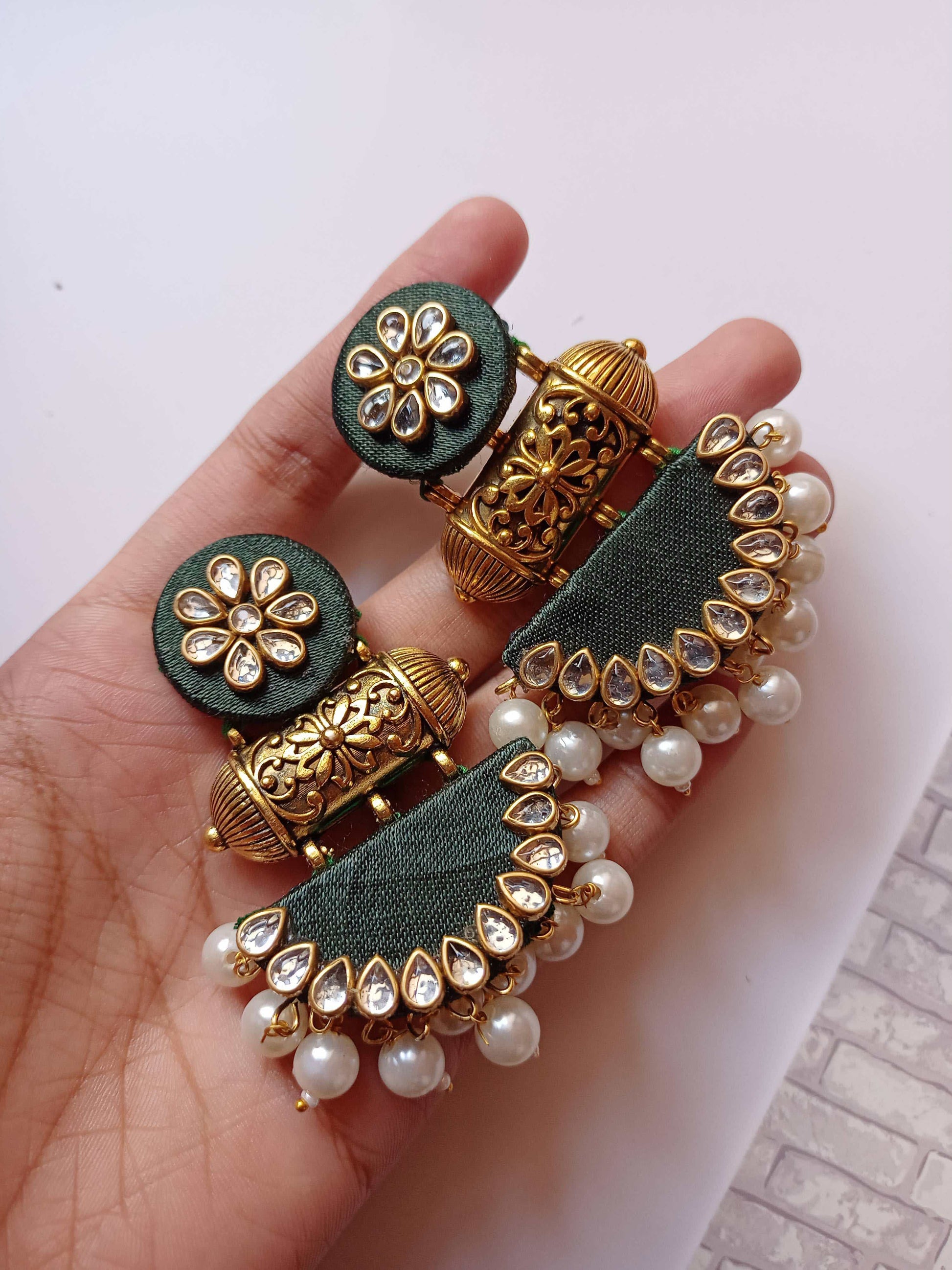 Palm holding Bottle green earrings with golden kundan and pearls work on white grey backdrop