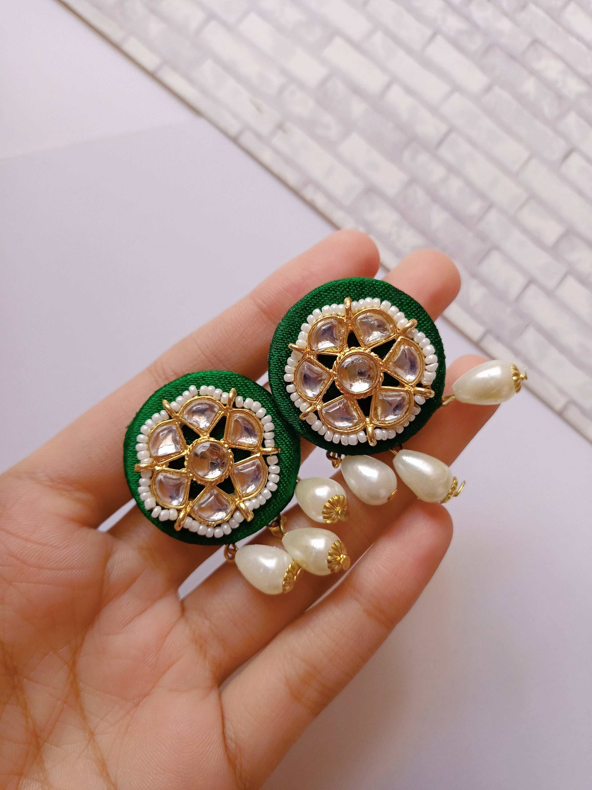 Palm holding Green round studs earrings with white beads and pearls latkan on white backdrop