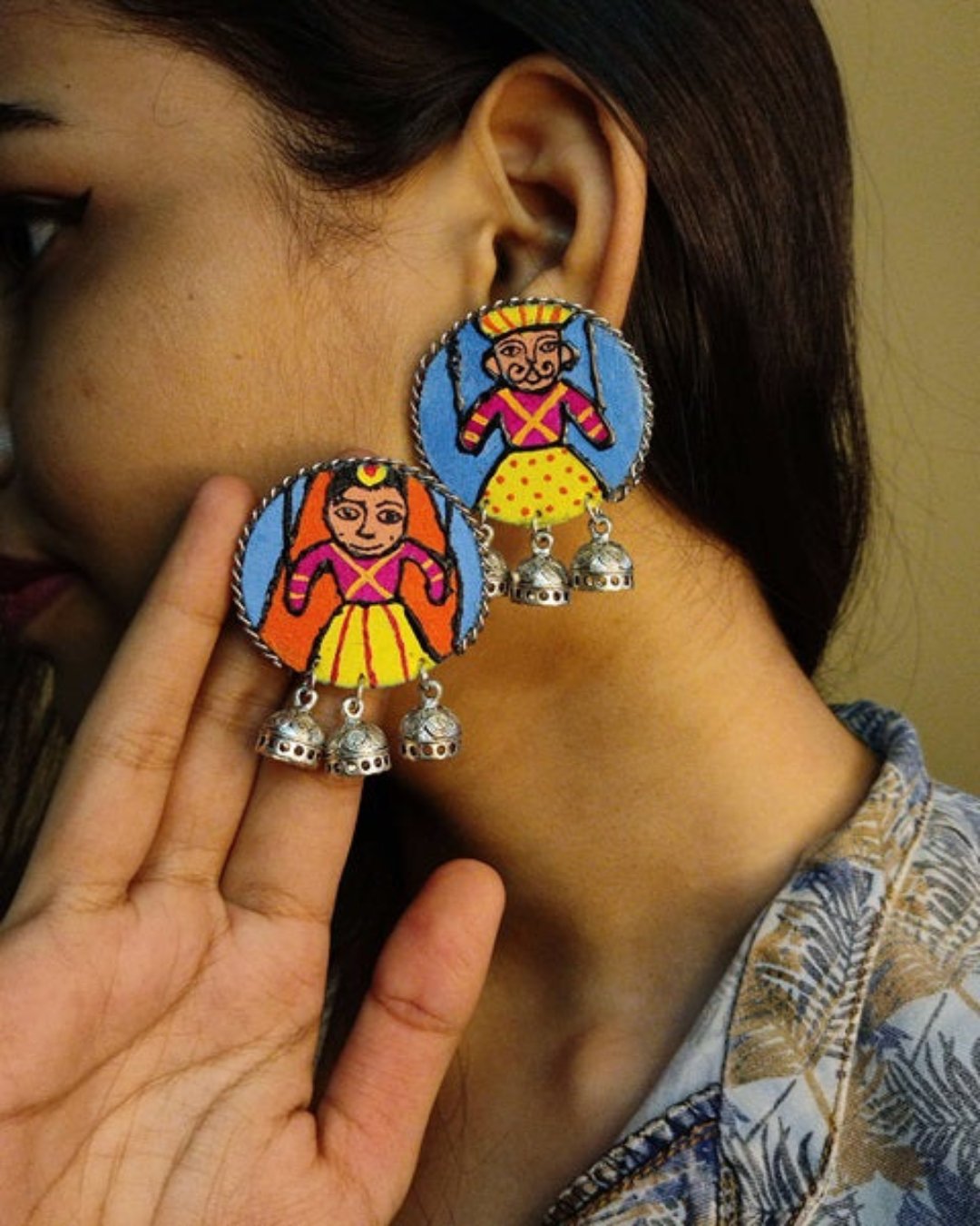 Girl wearing and holding round wooden Indian traditional earrings with Rajasthani gudda guddi painted 