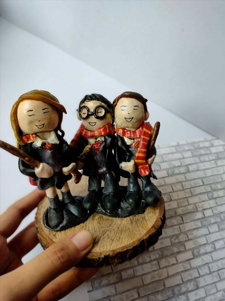 Hand holding Harry potter trio clay sculpture miniature on wooden base on white grey backdrop