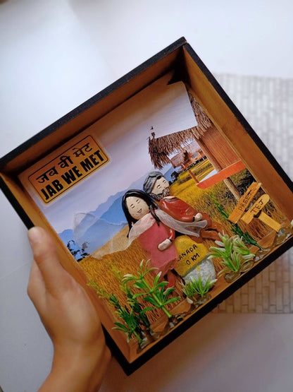 Hand holding Punjabi couple caricature pebble art inside a wooden frame on white grey backdrop