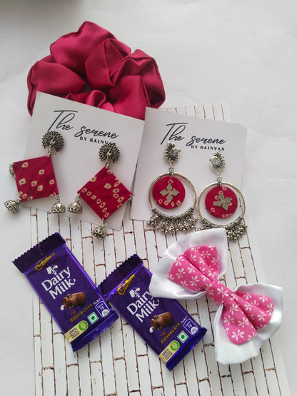 Brown box with multiple earrings, chocolates, dry fruits, hair scrunchies on white backdrop