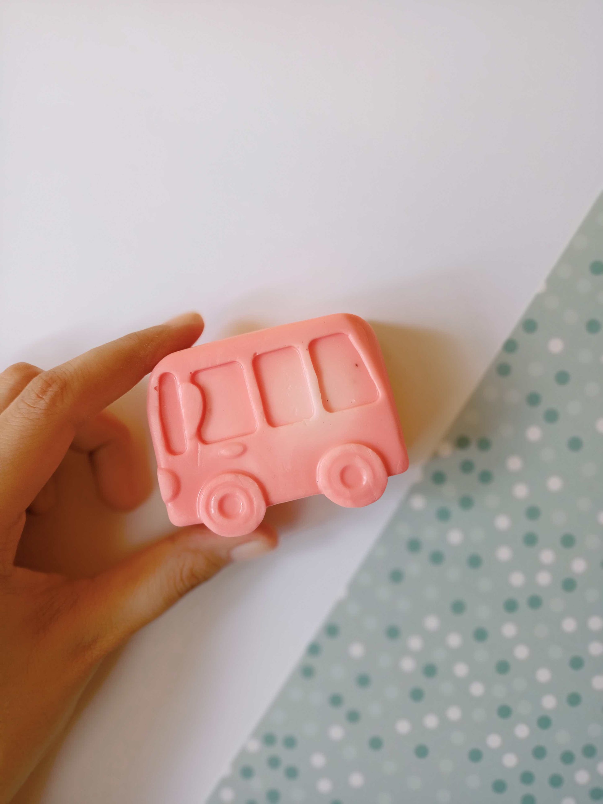 Hand holding Pink car shaped soap on blue white backdrop
