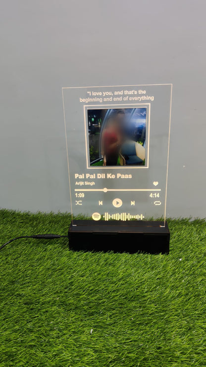 Rectangular frame with photo, LED light, spotify link and wooden base kept on green grass