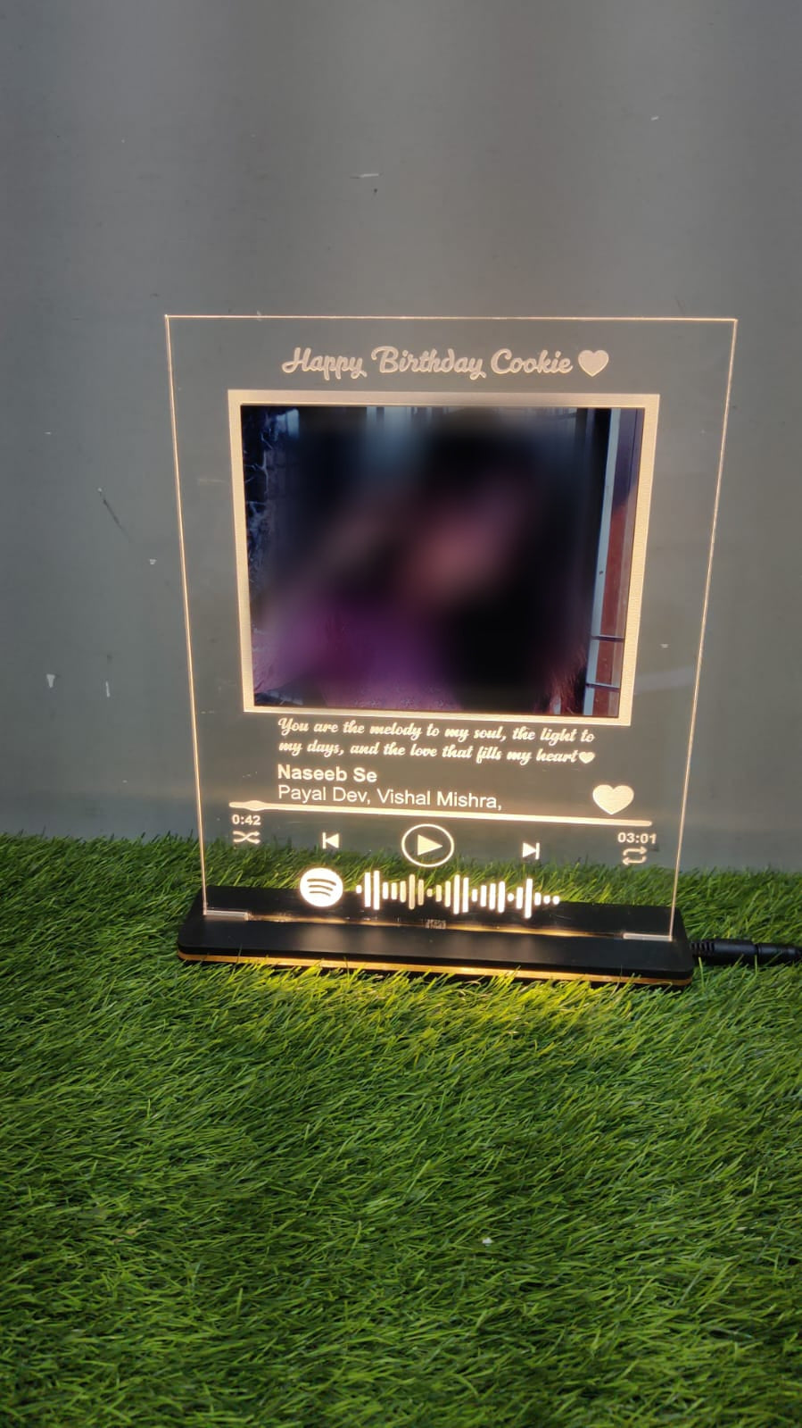 Rectangular LED frame with blurred photo and golden engraving kept on green grass