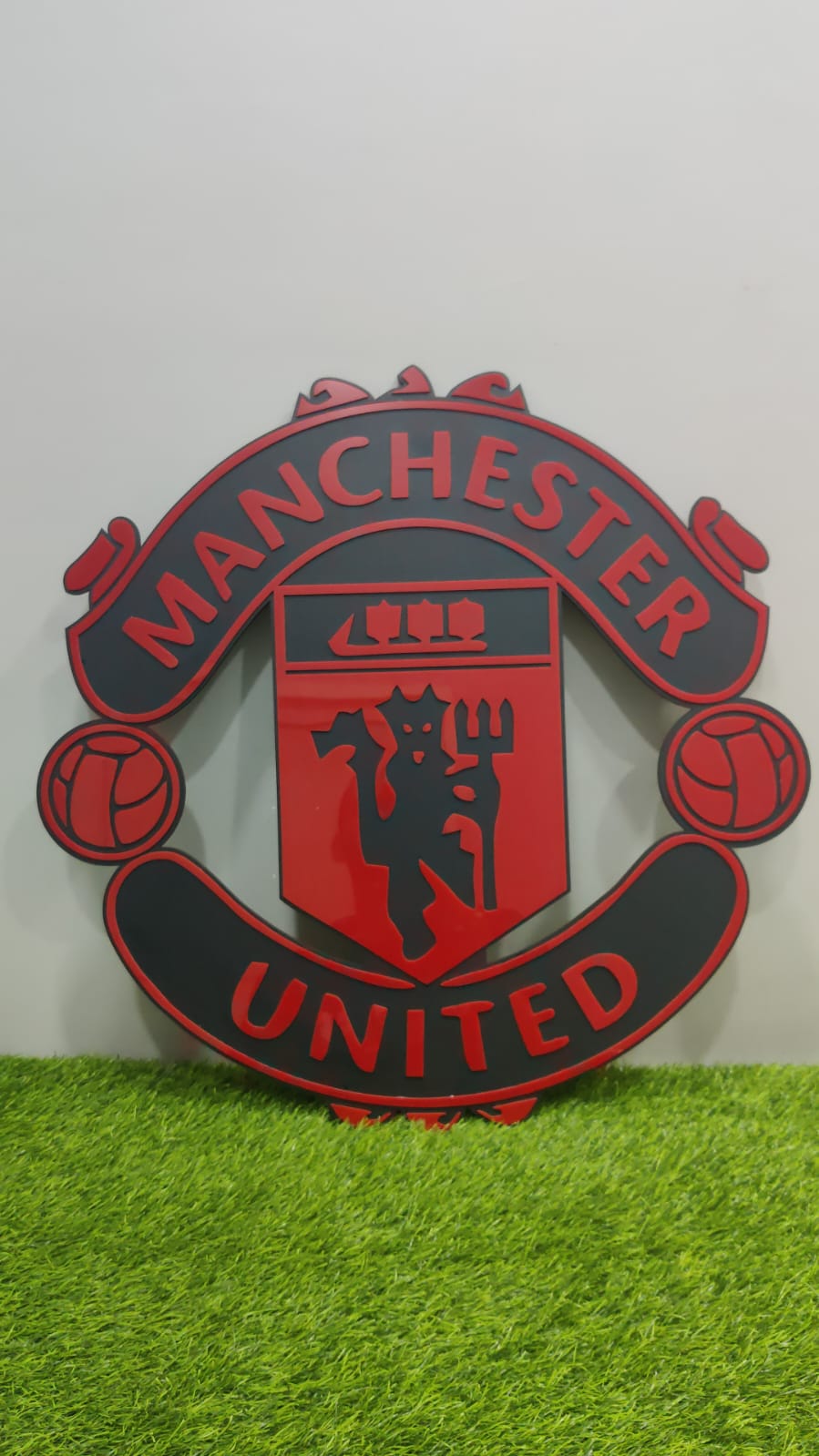 Red and black MDF wall art of Manchester united soccer team on green grass