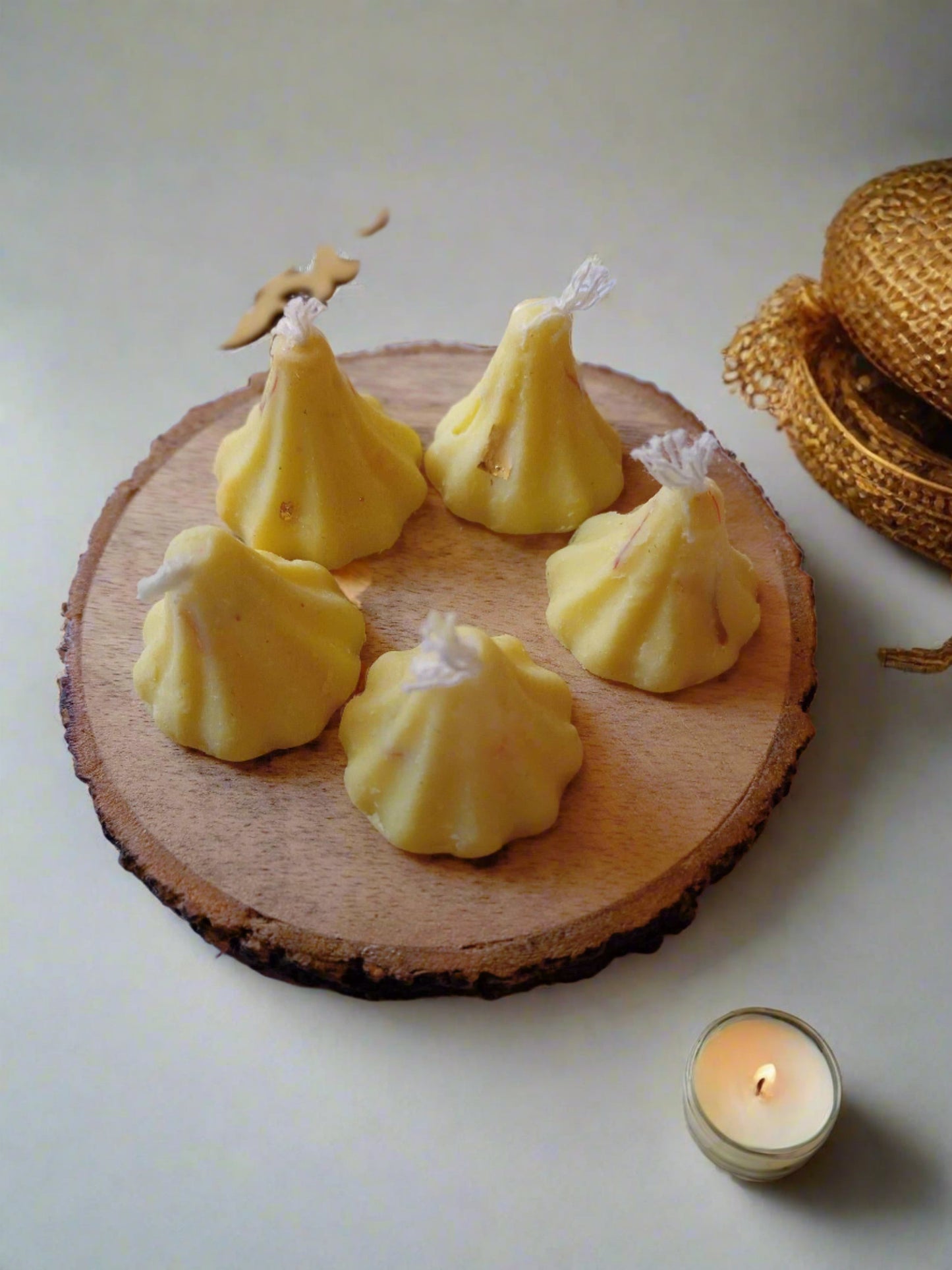 5 Modak shaped candles on wooden coaster with colorful props around
