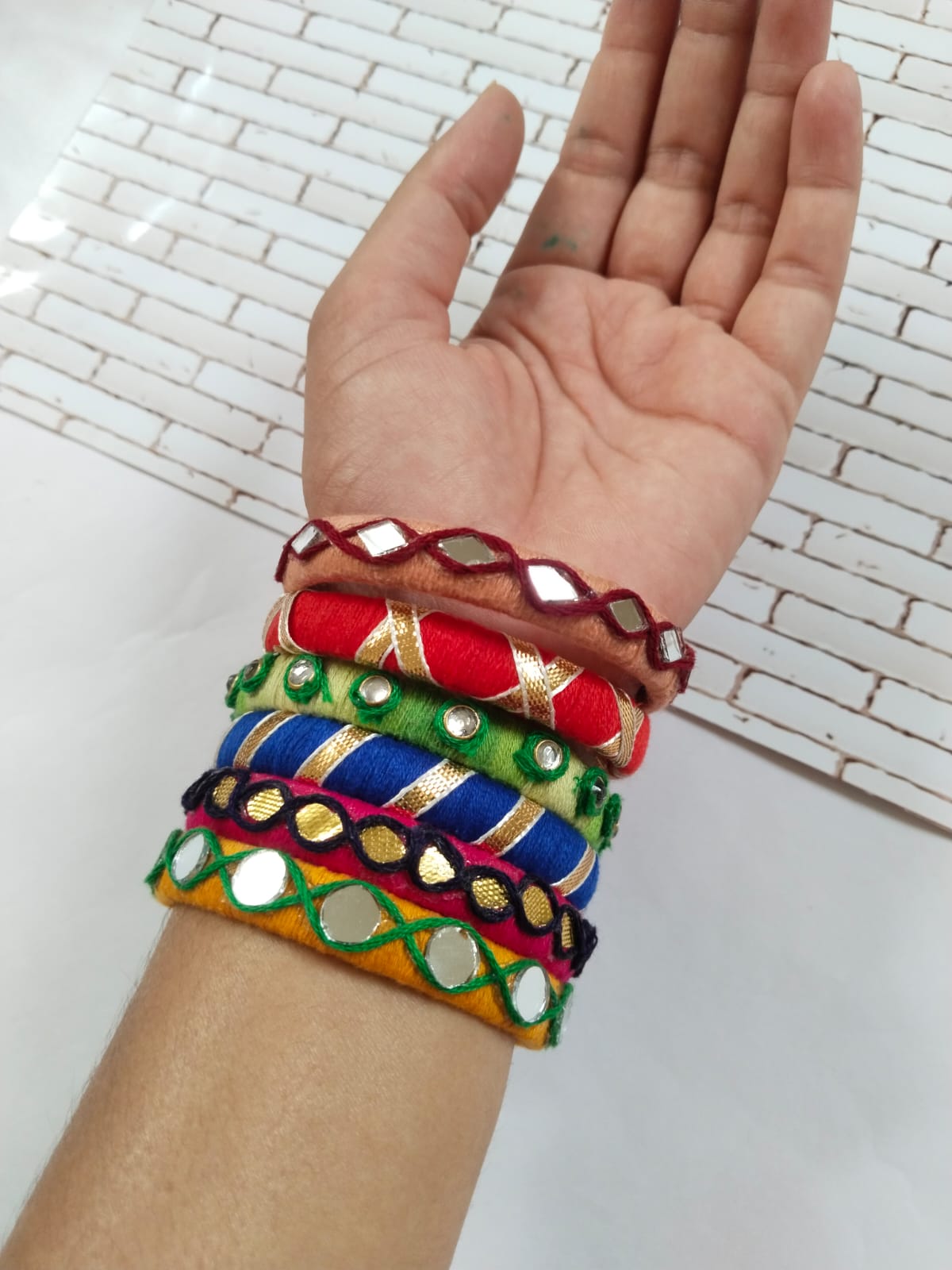 Hand wearing Multicolor multiple bangles on white grey backdrop