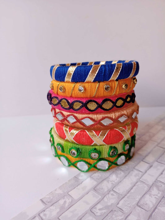 Pink and orange fabric bangles set with golden and silver mirror work on white backdrop