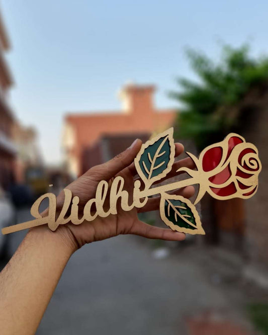 A hand holding wooden rose name stick with in brown and red