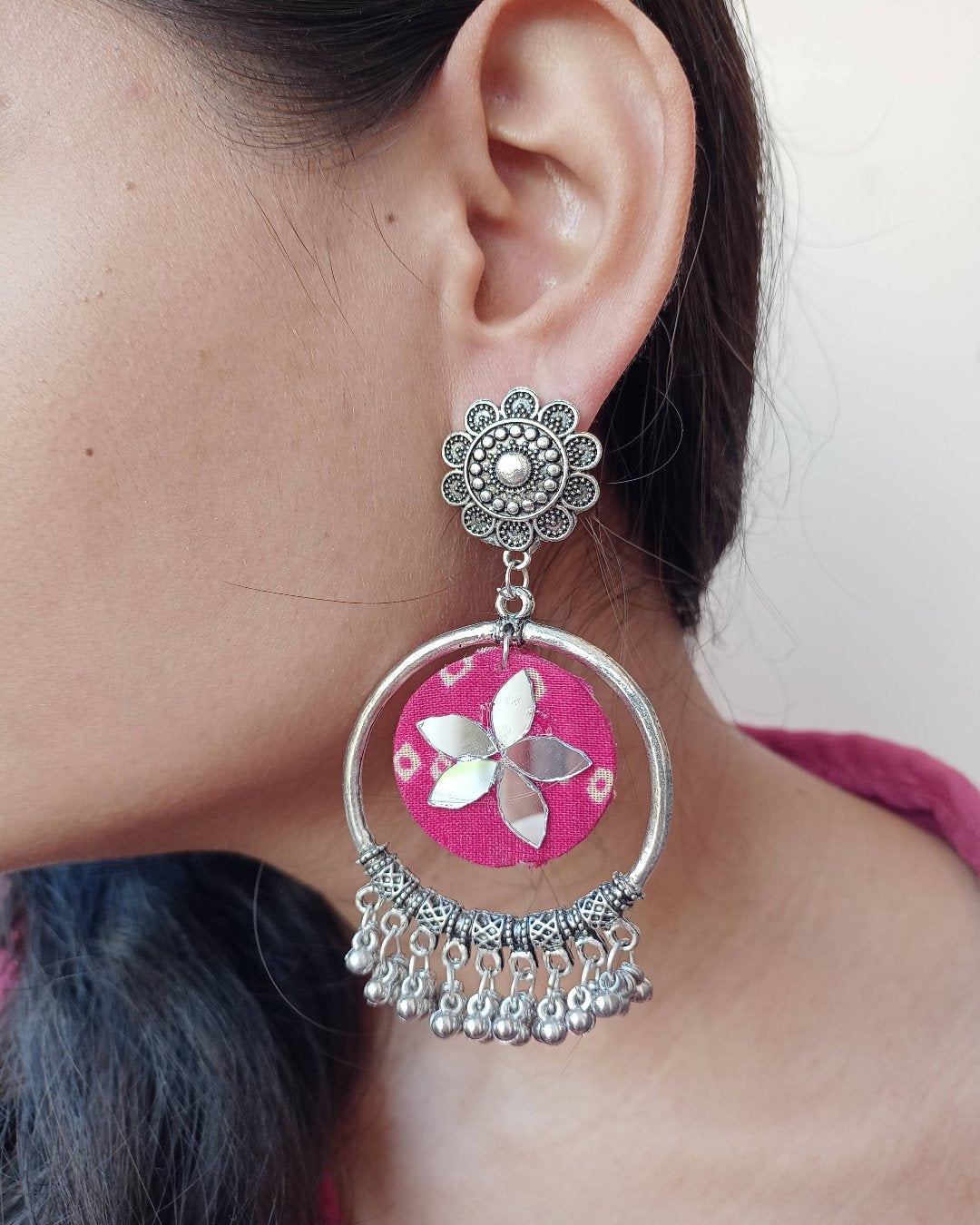 Close up of ear of a girl wearing Pink bandhani print jhumka bali earrings on white and grey backdrop