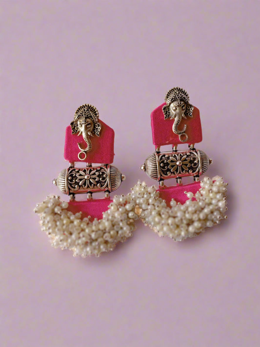 Pink earrings with ganpati face charm and silver white beads at the bottom on white grey backdrop