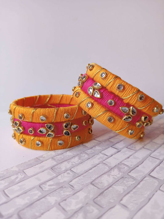 Pink and orange fabric bangles set with golden work on white backdrop
