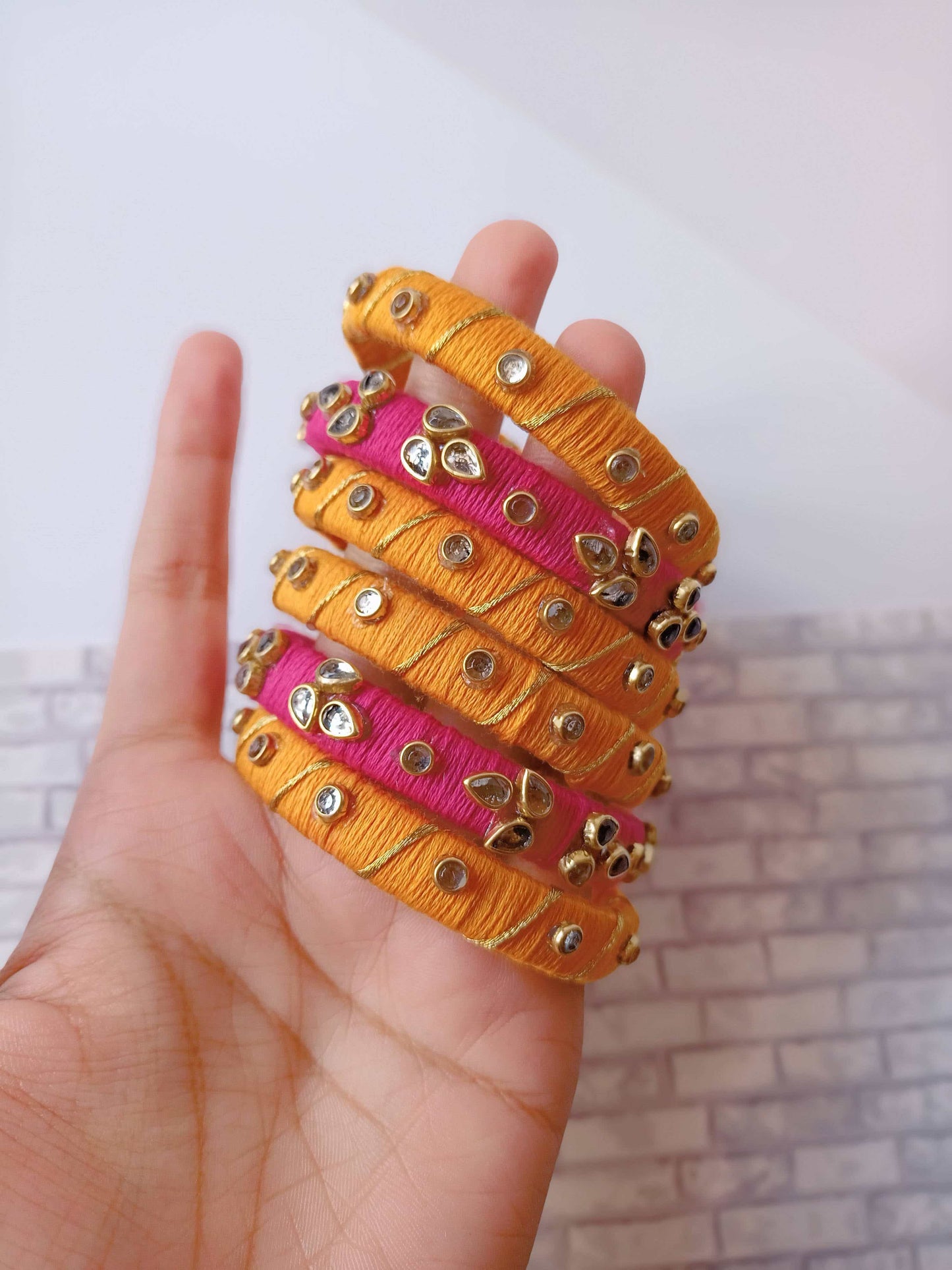 Palm holding pink and orange fabric bangles set with golden work on white backdrop