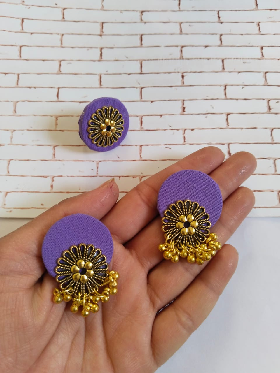 Palm holding Purple earrings and ring in round shapes with golden charms on white grey backdrop