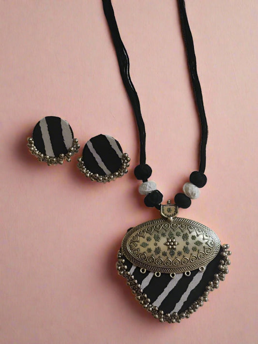 Black and white printed necklace and earrings set with silver locket on white backdrop