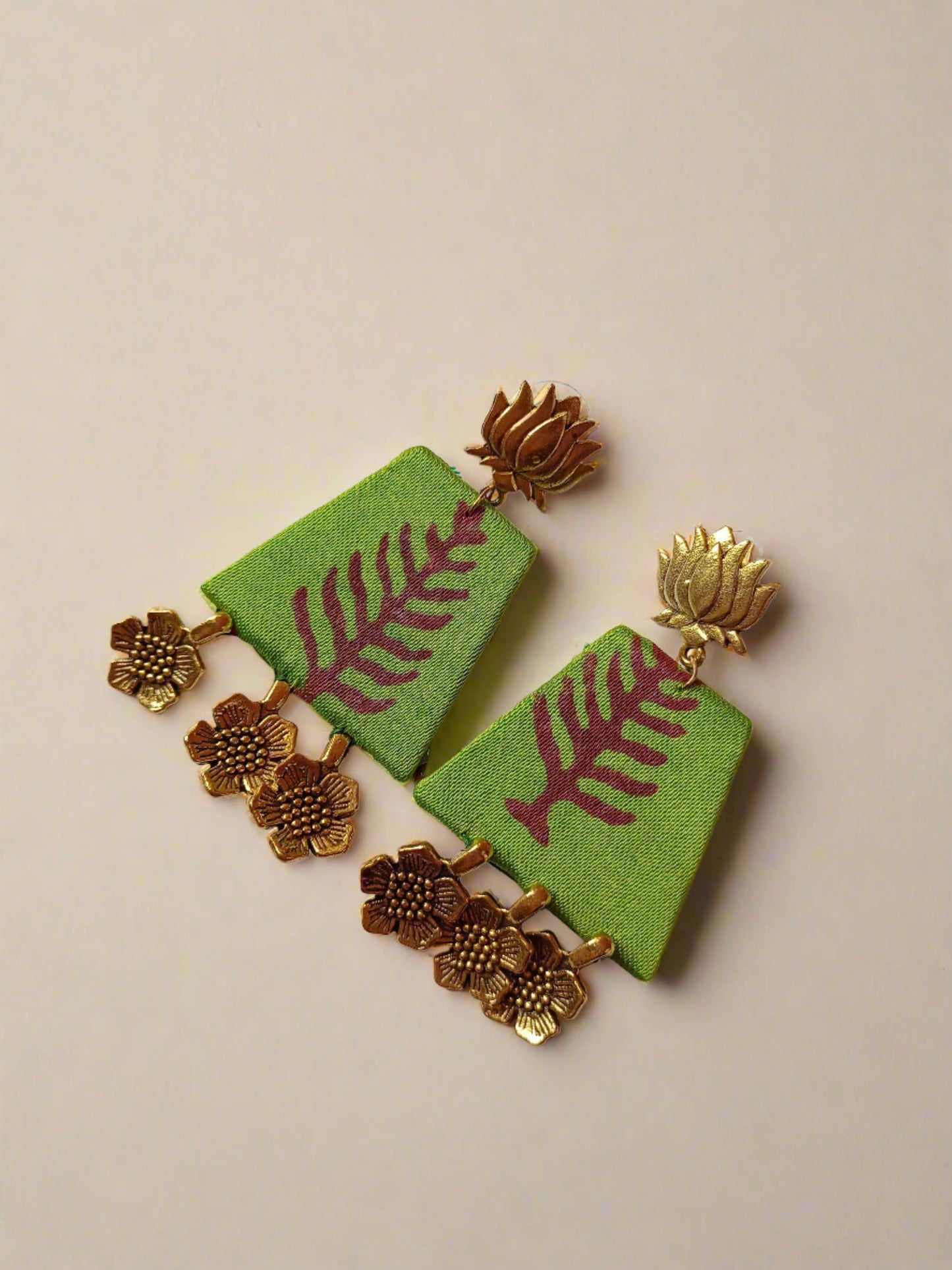 Green printed jhumka earrings with golden top in lotus shape and floral golden bottom on white backdrop