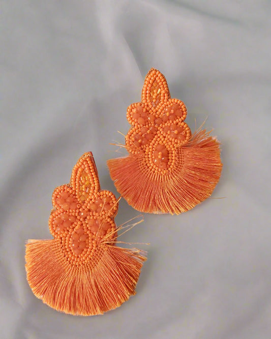 Orange floral beaded earrings with tassels on bottom on white backdrop