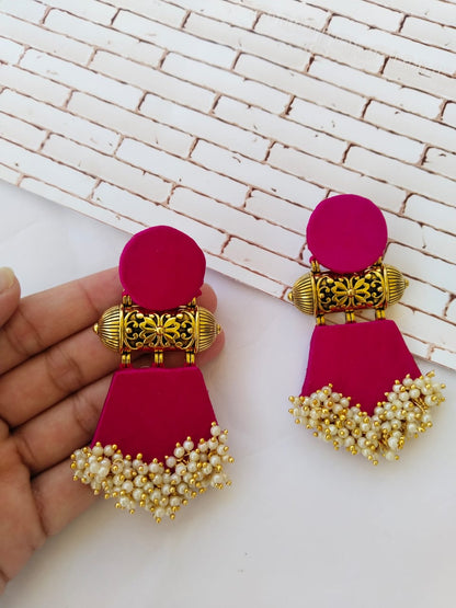 Fingers holding pink earrings with golden tabiz, white beads on white backdrop