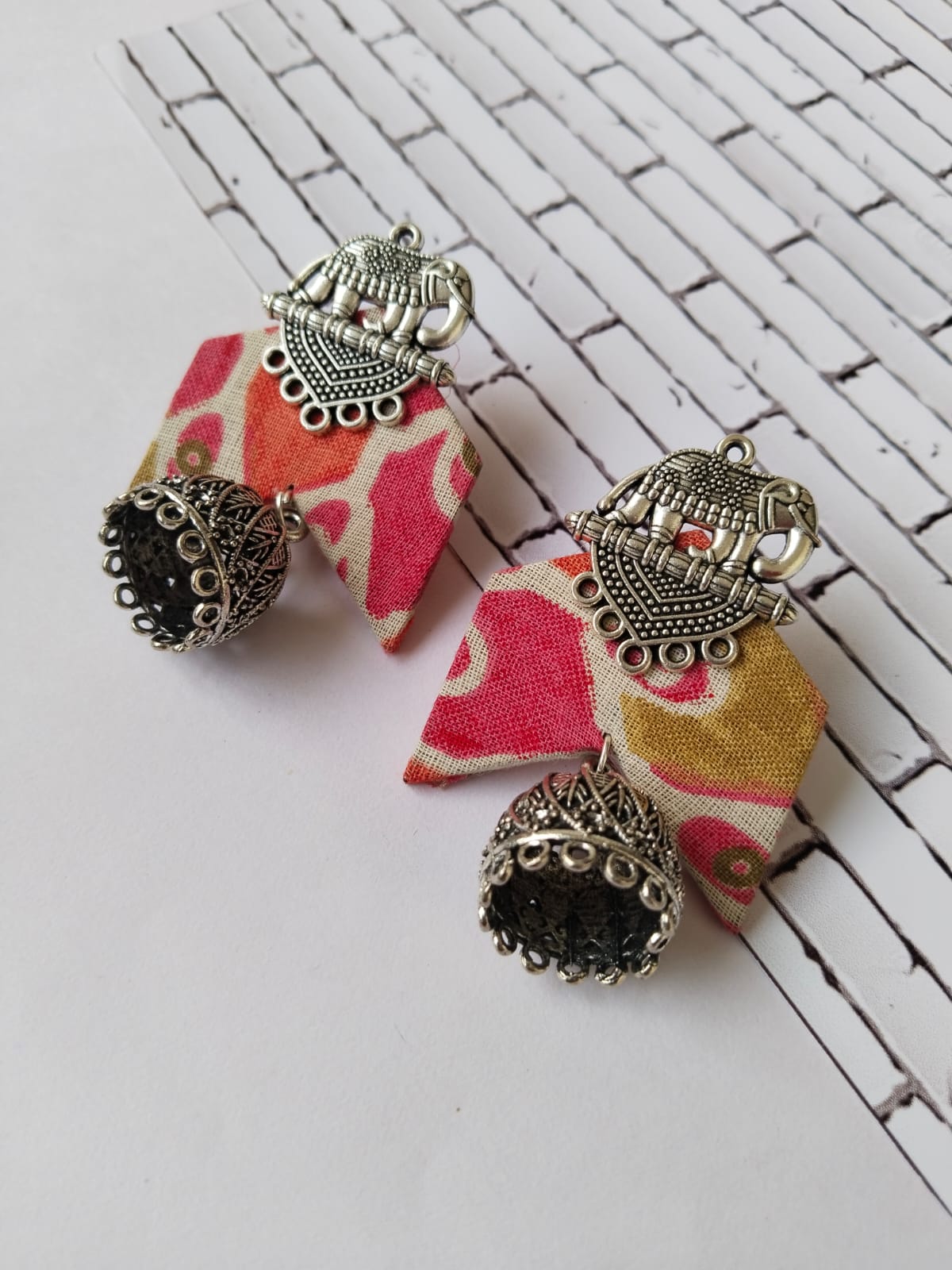 Pink floral printed earrings with silver charm on white backdrop