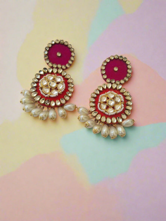 Round pink earrings with kundan border with pearls at bottom on white backdrop