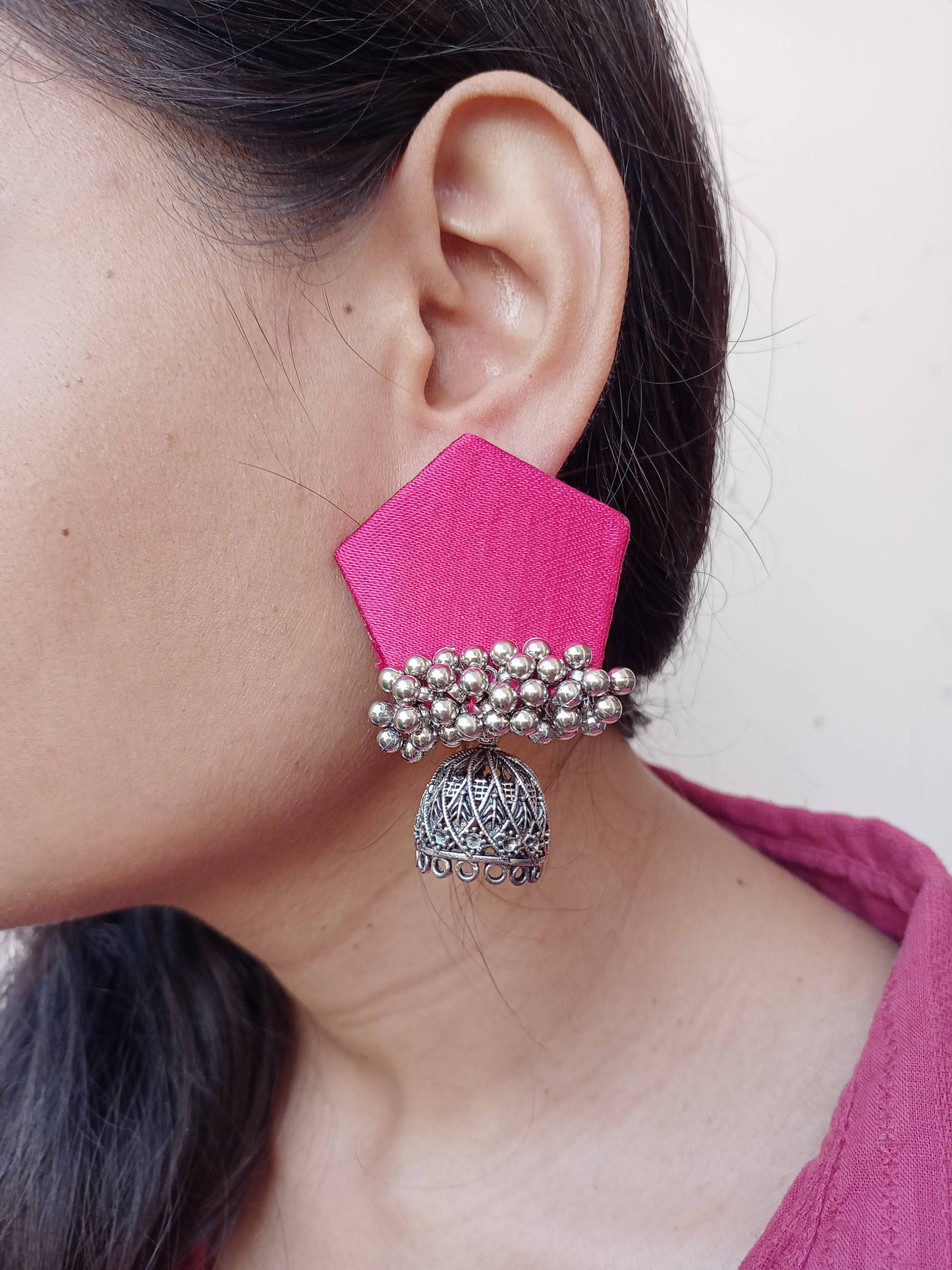 Close up of an ear of a girl wearing pink pentagon earrings with silver ghungroo and charm