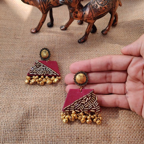 Maroon red earrings with golden ghungroos and beads on brown backdrop