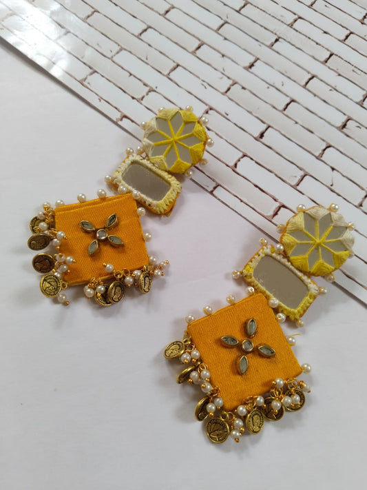 Yellow earrings with golden beads, mirror and coins on a white backdrop