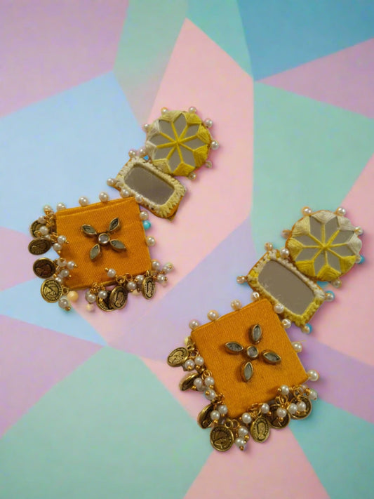 Yellow earrings with golden beads, mirror and coins on a white backdrop