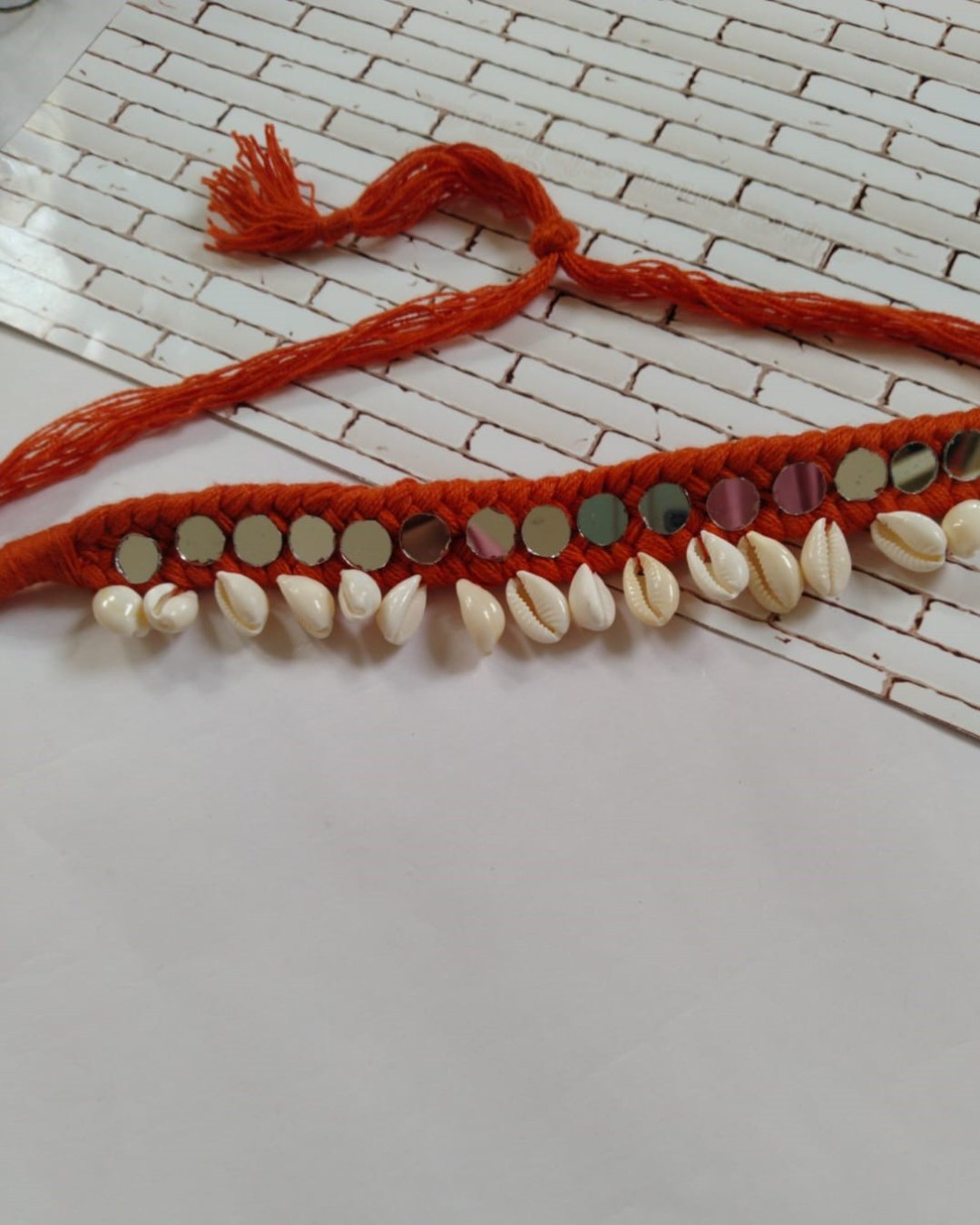 Red woven choker necklace with mirrors and white sea shells on white backdrop