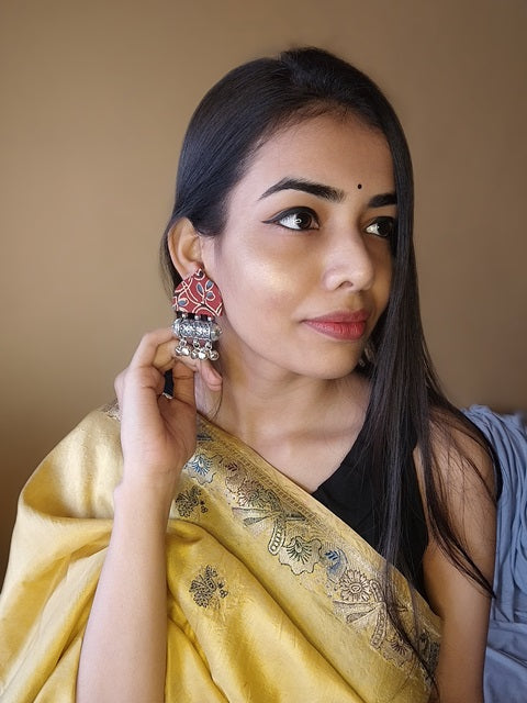 Indian brown woman smiling wearing yellow saree and red printed earrings with silver ghungroos
