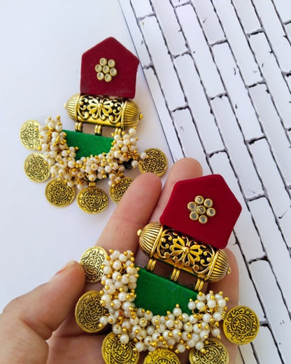 Fingers holding red and green earrings with golden coins and white beads