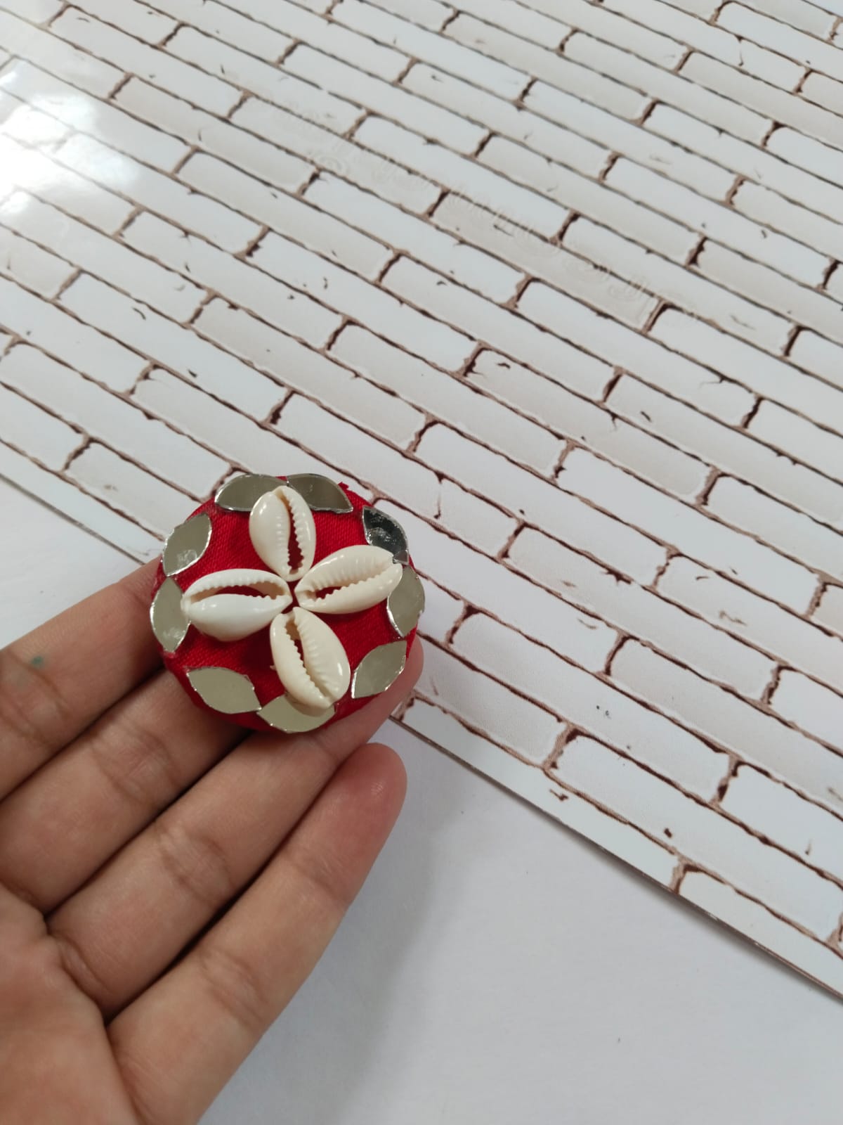 Finger holding red ring with mirrors and white sea shells