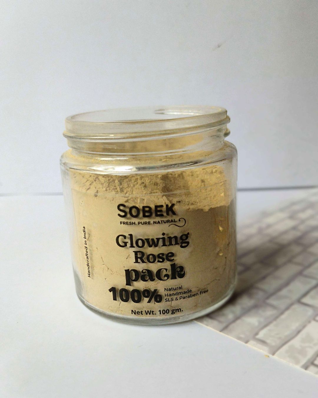 Glass jar with sobek brown rose face pack on white wall