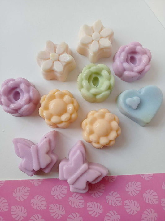 Mini flowers and butterfly shaped colorful soaps on white pink backdrop